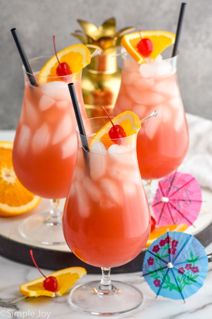 Photo of three Sex on the Beach cocktails garnished with orange slice and cherry with straws for drinking. Extra fruit and umbrellas for garnish