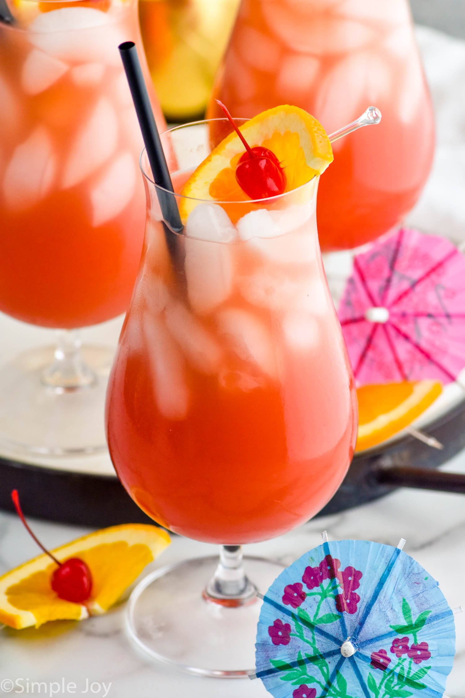 Photo of Sex on the Beach garnished with orange slice and cherry. Extra fruit and umbrellas beside glass for garnish.