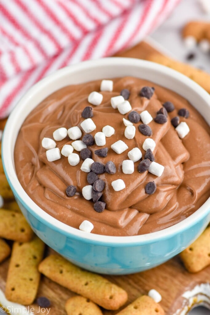 Photo of a bowl of S'mores Dip garnished with mini marshmallows and chocolate chips with graham crackers beside bowl for dipping.