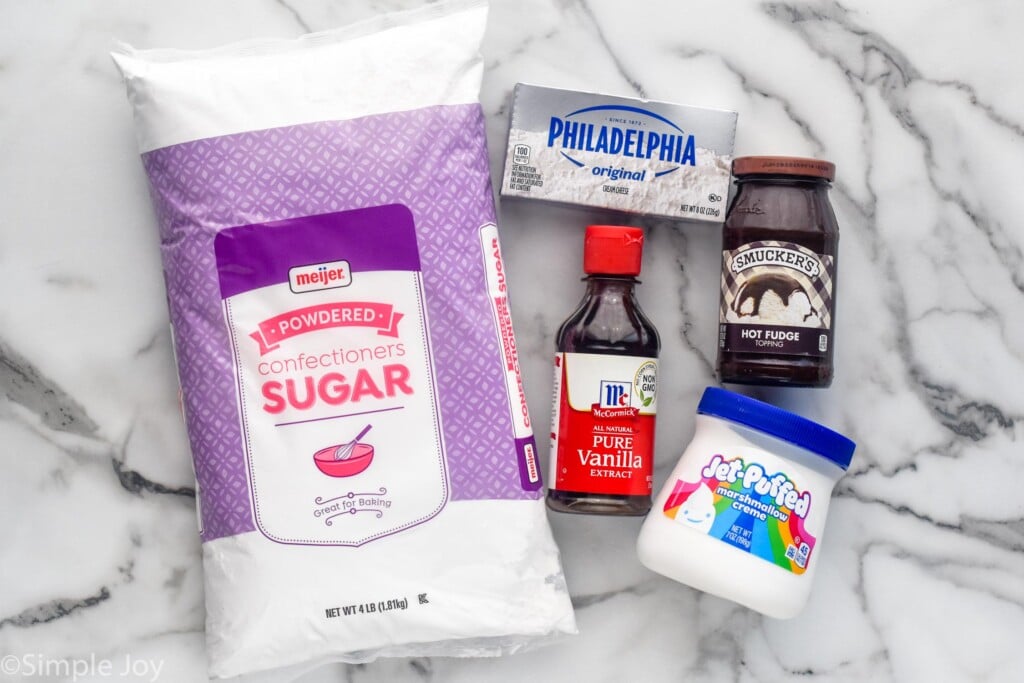 Overhead photo of ingredients for S'mores Dip on counter, including powdered sugar, vanilla extract, cream cheese, hot fudge, and marshmallow cream.