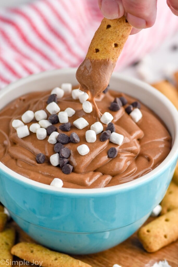 Photo of person's hand dipping a graham cracker into a bowl of S'mores Dip