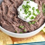 Pinterest graphic for black bean dip. Image shows bowl of black bean dip topped with sour cream and cilantro with tortilla chips surrounding. Text says "black bean dip simplejoy.com"