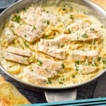 Pinterest graphic for Chicken Alfredo recipe. Image shows a skillet of Chicken Alfredo with glasses of wine and bread beside. Text says, "Chicken Alfredo simplejoy.com"