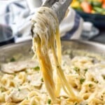 Pinterest graphic for Chicken Alfredo recipe. Text says, "the best Chicken Alfredo simplejoy.com." Image shows tongs lifting Chicken Alfredo out of skillet