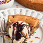 Pinterest graphic for Cookie Cake recipe. Text says, "the best Cookie Cake simplejoy.com." Image shows a slice of Cookie Cake on a plate with a fork, garnished with ice cream and chocolate syrup.