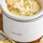 Pinterest image for corn dip. Image shows person's hand pulling chip with corn dip out of small crockpot of corn dip. Text says "super easy corn dip recipe simplejoy.com"