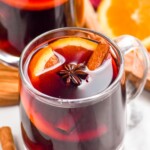 Photo of mugs of Slow Cooker Mulled Wine with cinnamon sticks and oranges beside