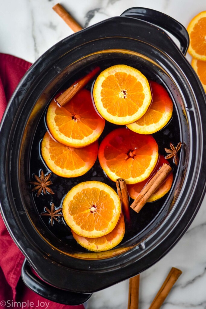 Overhead photo of a crock pot of Slow Cooker Mulled Wine with cinnamon sticks and orange slices beside