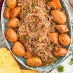 Pinterest graphic for Slow Cooker Pot Roast recipe. Image is overhead photo of a platter of Slow Cooker Pot Roast and potatoes. Wine and toast beside platter. Text says, "super easy crockpot pot roast simplejoy.com"