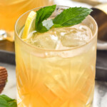 Photo of a Whiskey Smash garnished with mint leaves and lemon slice. Another Whiskey Smash and mint leaves beside.
