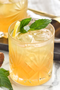 Photo of a Whiskey Smash garnished with mint leaves and lemon slice. Another Whiskey Smash and mint leaves beside.