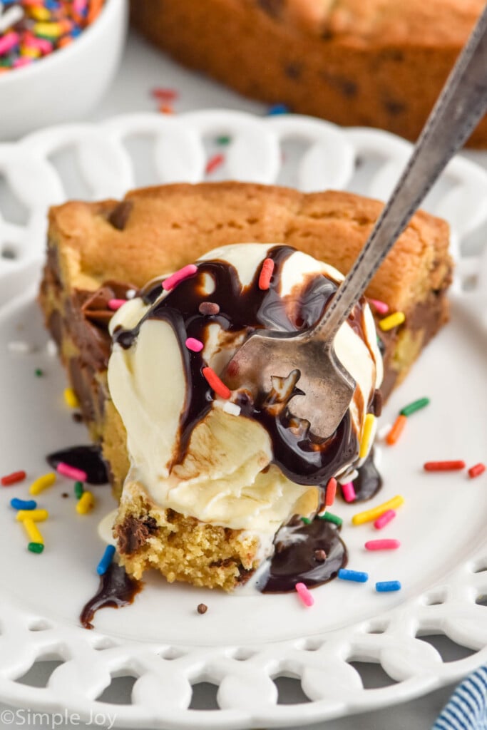 Photo of a fork digging into a slice of Cookie Cake garnished with ice cream and chocolate syrup.