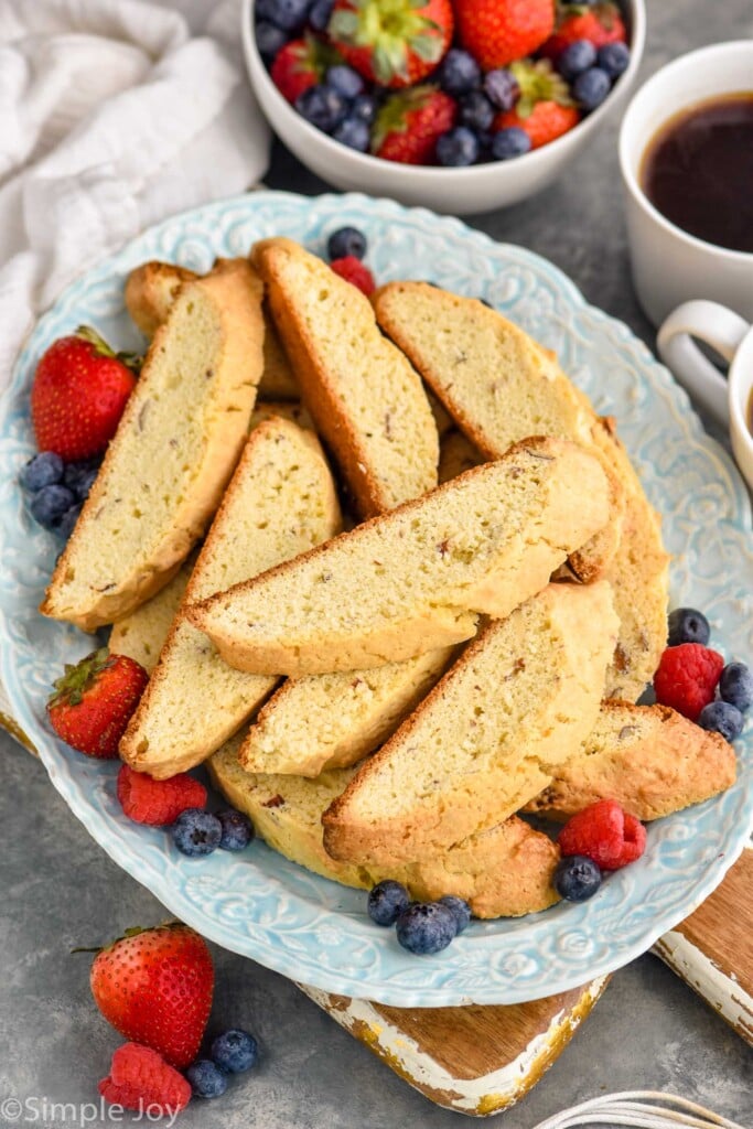 Overhead photo of a plate of Biscotti with fruit. Bowl of fruit and cup of coffee beside.