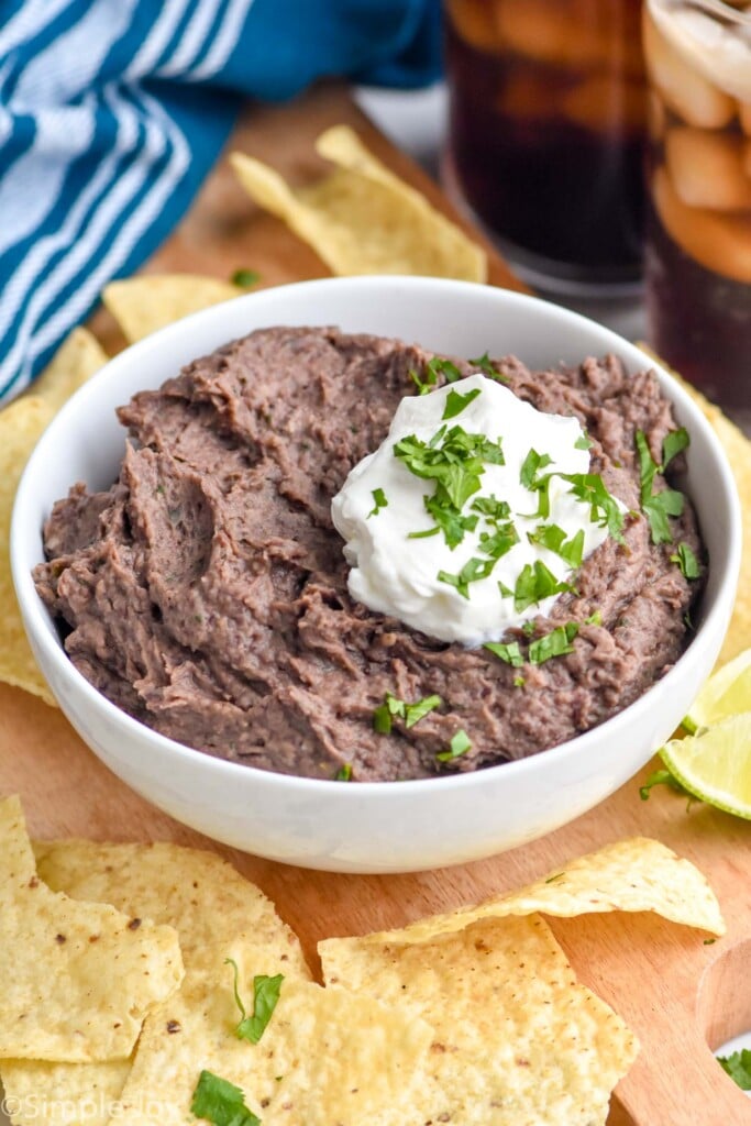 bowl of black bean dip topped with sour cream and cilantro with tortilla chips surrounding