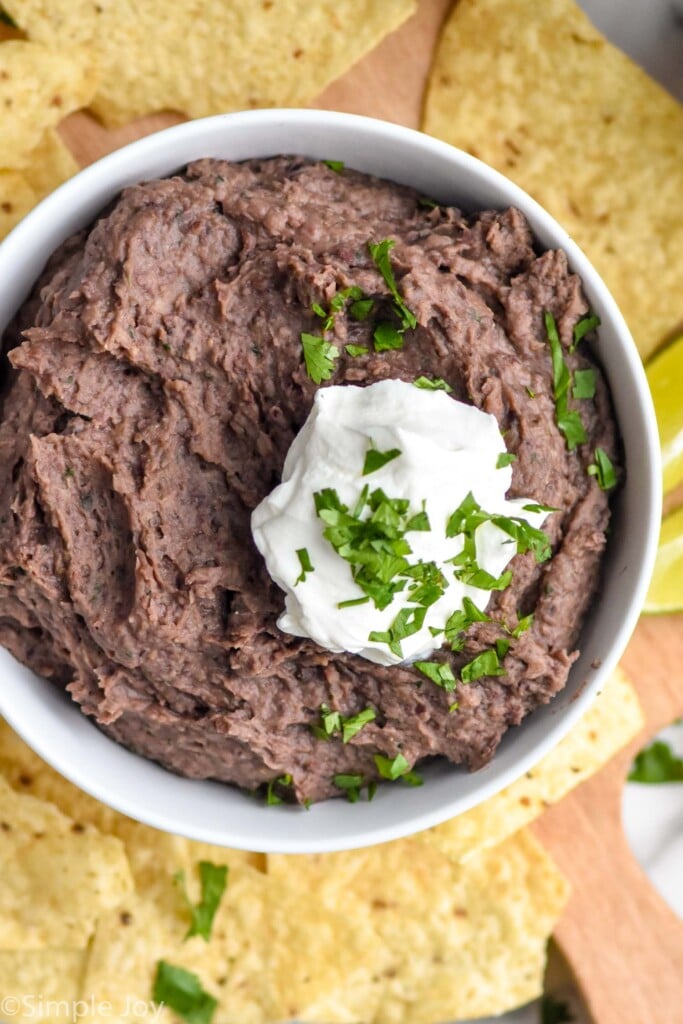 bowl of black bean dip topped with sour cream and cilantro with tortilla chips surrounding