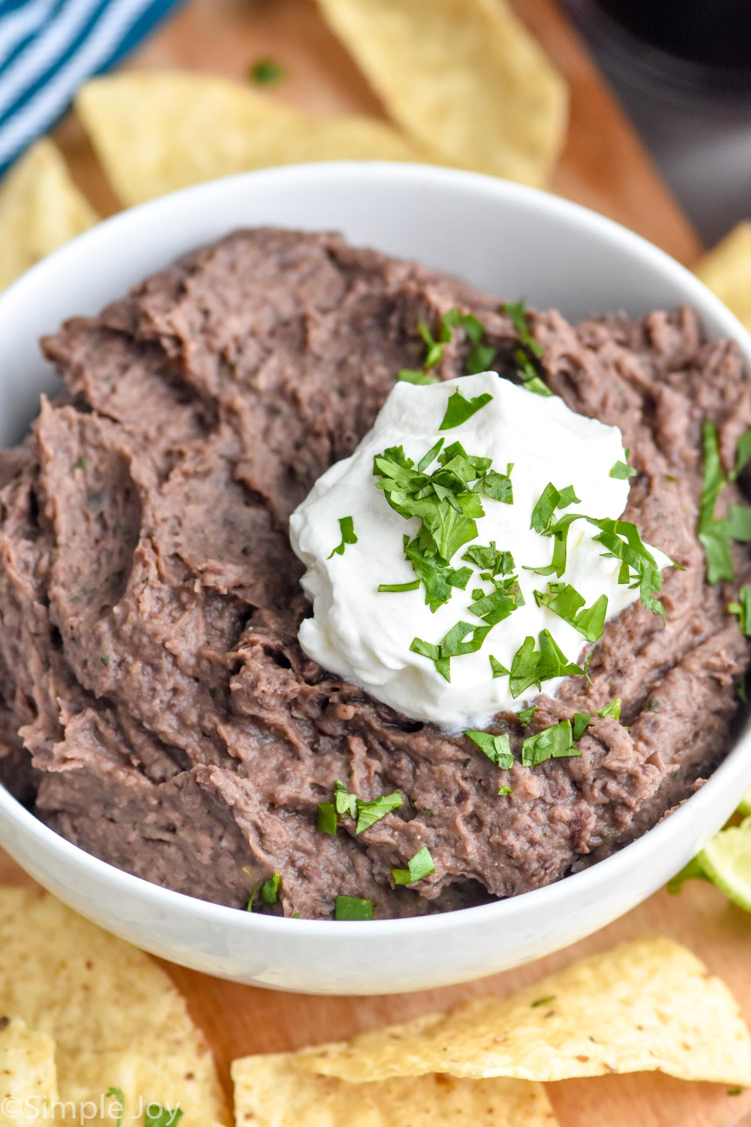 bowl of black bean dip topped with sour cream and cilantro with tortilla chips surrounding