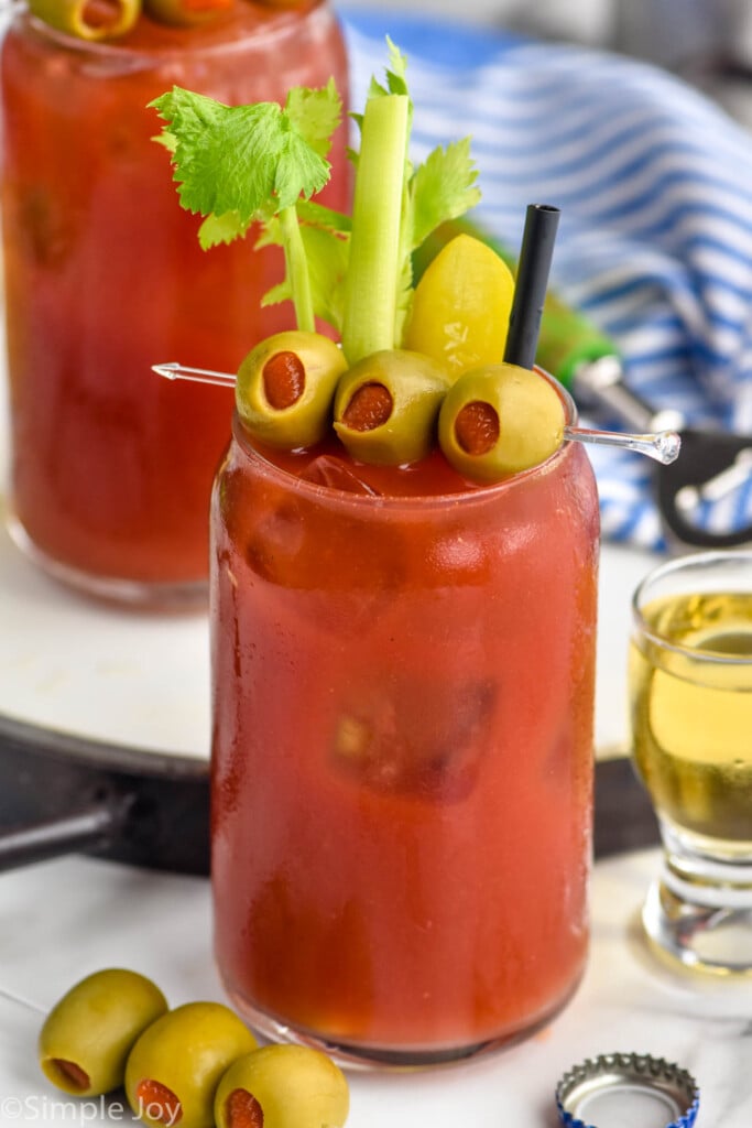 Photo of Bloody Mary garnished with olives, celery, and pickles. Shot of beer and another spear of olives beside.