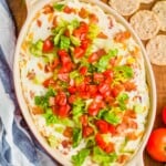 overhead view of blt dip in an oval ceramic baking dish on a wood board with round crackers around it