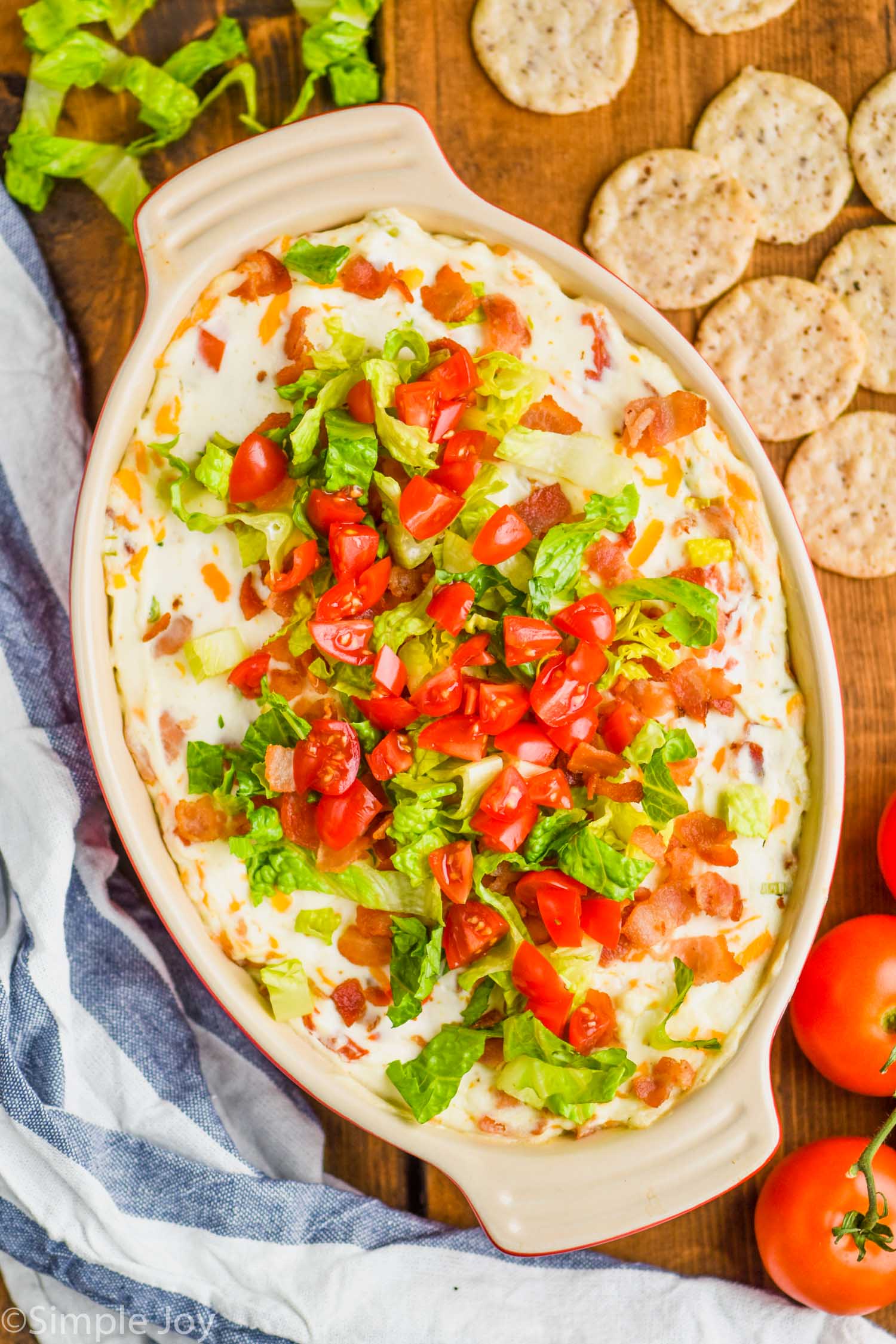 overhead view of blt dip in an oval ceramic baking dish on a wood board with round crackers around it