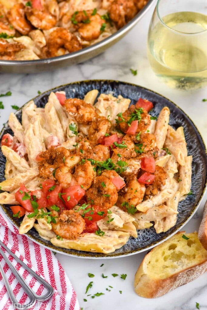 plate of Cajun Shrimp Pasta with glass of white wine and garlic bread sitting beside