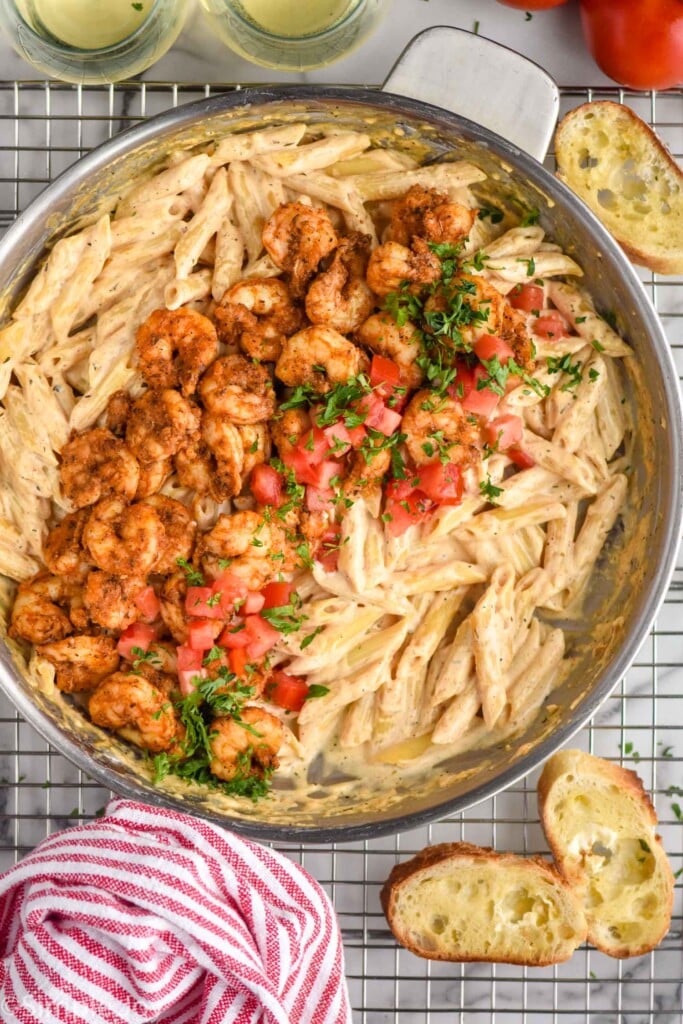 overhead of skillet of Cajun Shrimp Pasta ingredients on a cooling rack with toasted bread sitting beside