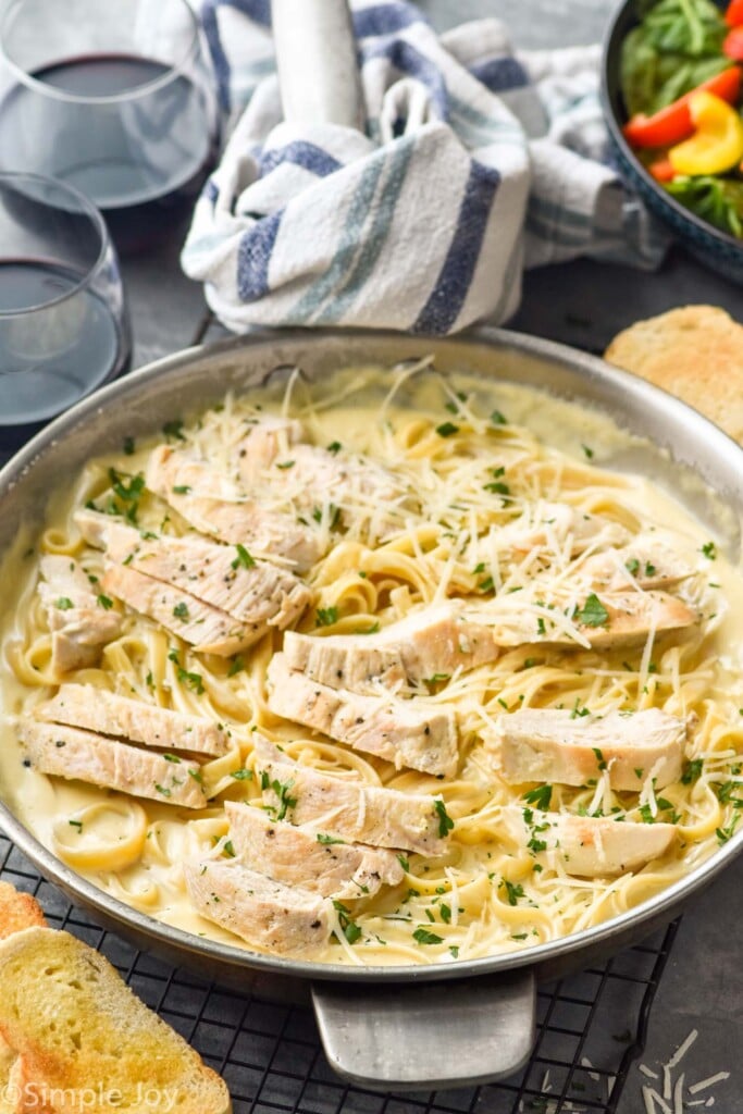 Photo of a skillet of Chicken Alfredo with wine and salad beside