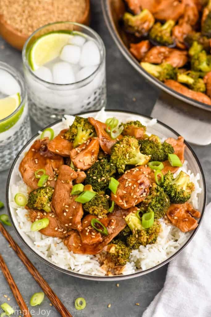 Photo of Chicken and Broccoli Recipe served on rice. Two drinks and pan of Chicken and Broccoli Recipe beside.