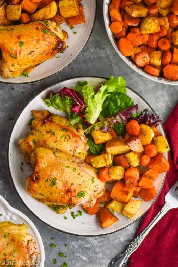 Overhead photo of plates of Baked Chicken Thighs with side salad and veggies.