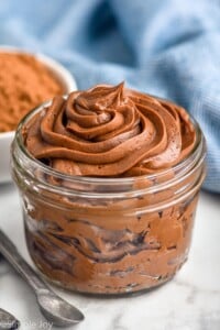 glass jar of chocolate frosting with measuring spoons