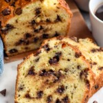 Photo of a partially sliced loaf of Chocolate Chip Bread with cups of coffee and chocolate chips beside