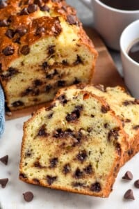 Photo of a partially sliced loaf of Chocolate Chip Bread with cups of coffee and chocolate chips beside