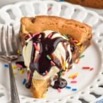 Photo of a slice of Cookie Cake served on a plate and garnished with ice cream and chocolate syrup. Fork for serving. - 10