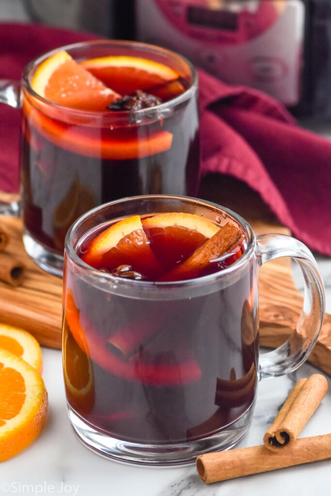Photo of two mugs of Slow Cooker Mulled Wine with cinnamon sticks and orange slices beside.