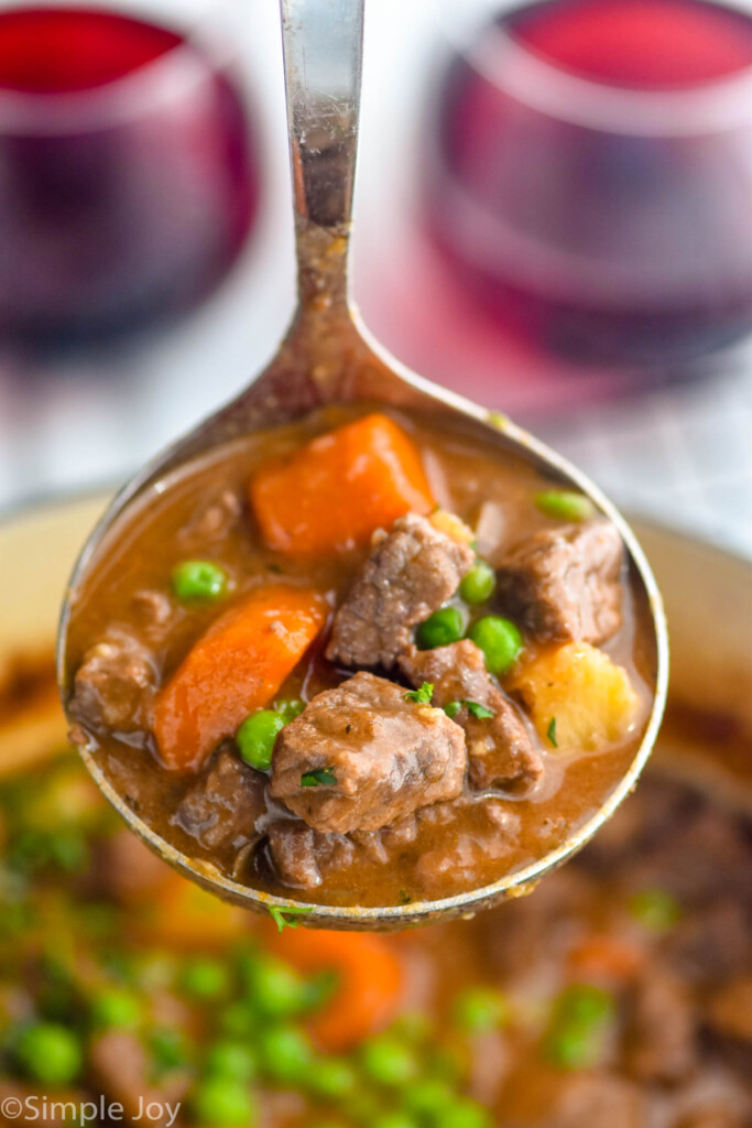 Close up photo of a ladle of Beef Stew with two glasses of wine in the background