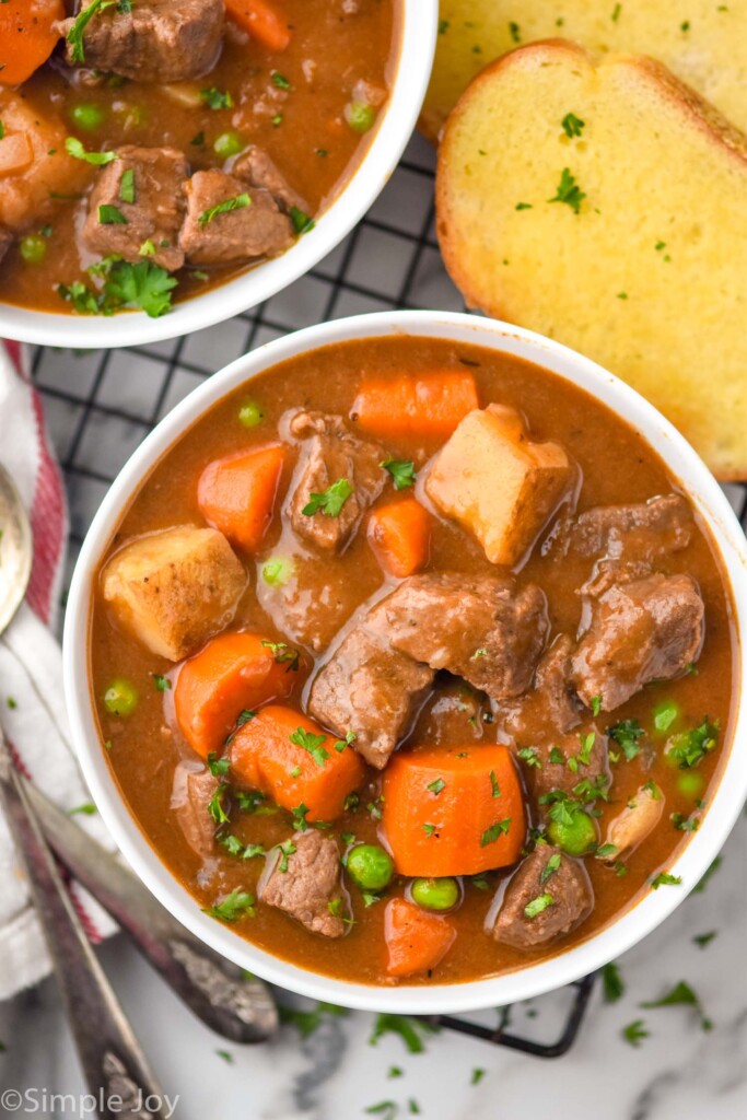 Overhead photo of two bowls of Beef Stew with spoons and garlic bread beside
