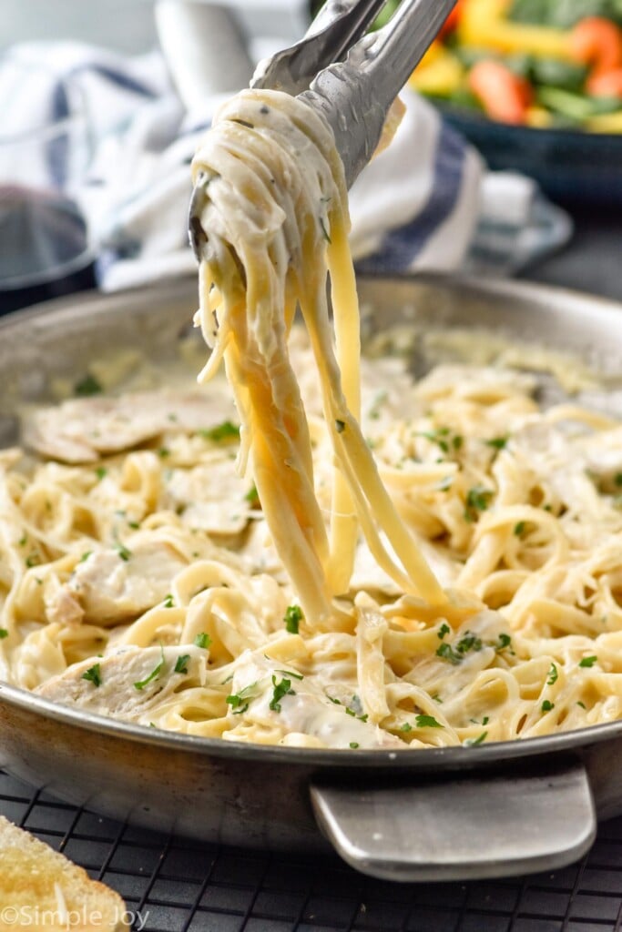Photo of tongs lifting Chicken Alfredo out of skillet