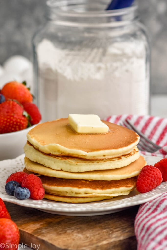 Plate of pancakes with butter and fresh berries. Container of homemade pancake mix sitting in background