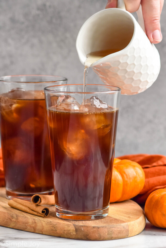 Photo of person's hand pouring pumpkin spice syrup into glass of cold brew coffee for Pumpkin Cream Cold Brew recipe.