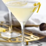 Side view of two Lemon Drop Martini cocktails garnished with lemon twist. Lemon slices beside glasses.
