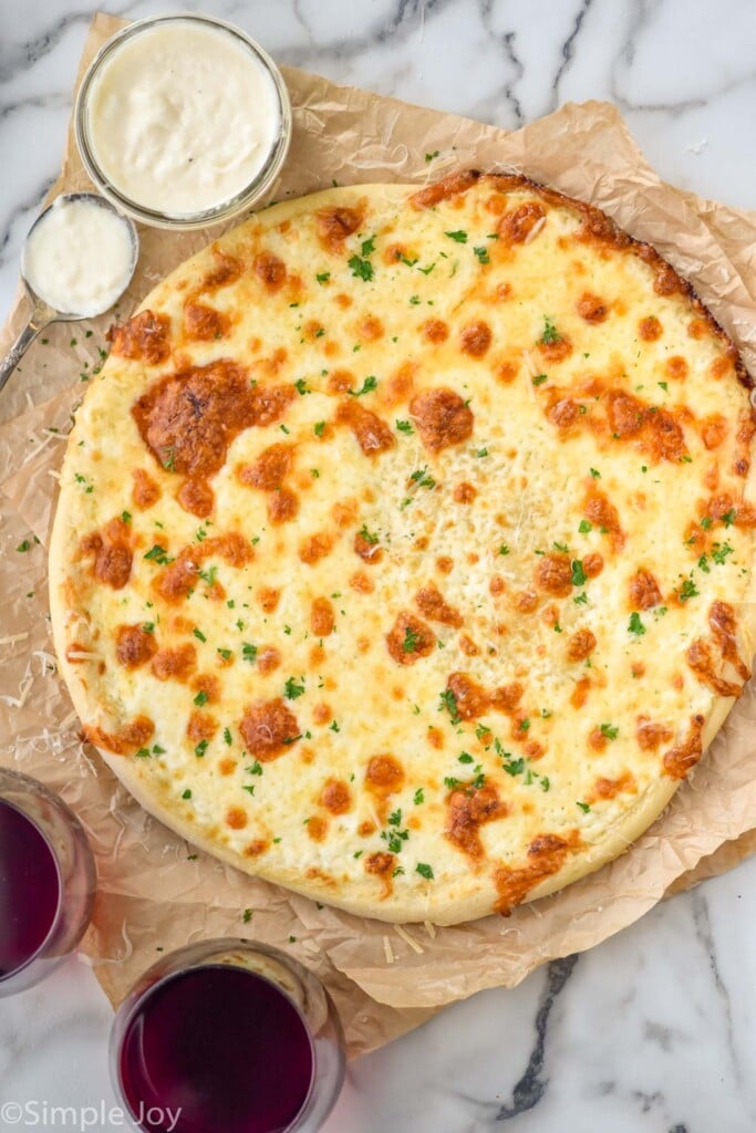 overhead of pizza with white pizza sauce. White sauce and two glasses of red wine sitting beside pizza