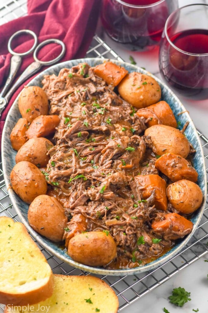 Photo of a platter of Slow Cooker Pot Roast and potatoes with wine and bread beside