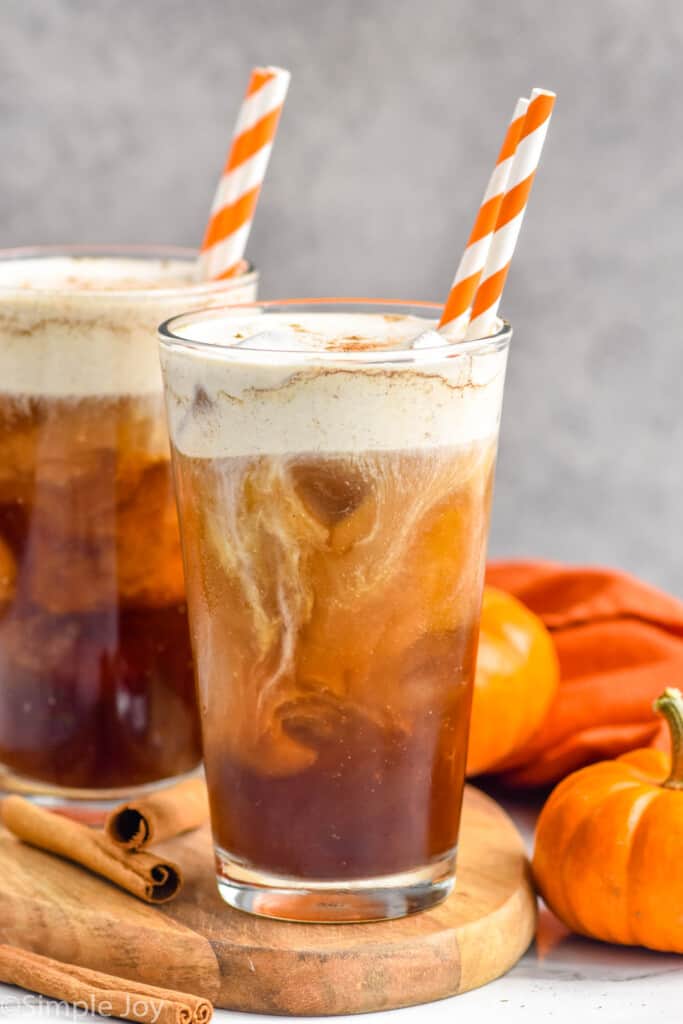 Side view of two glasses of Pumpkin Cream Cold Brew with straws. Pumpkins beside
