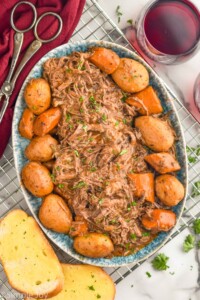 Overhead photo of a platter of Slow Cooker Pot Roast with potatoes. Wine and toast beside.