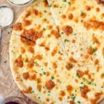 overhead of pizza with white pizza sauce. White sauce and two glasses of red wine sitting beside pizza
