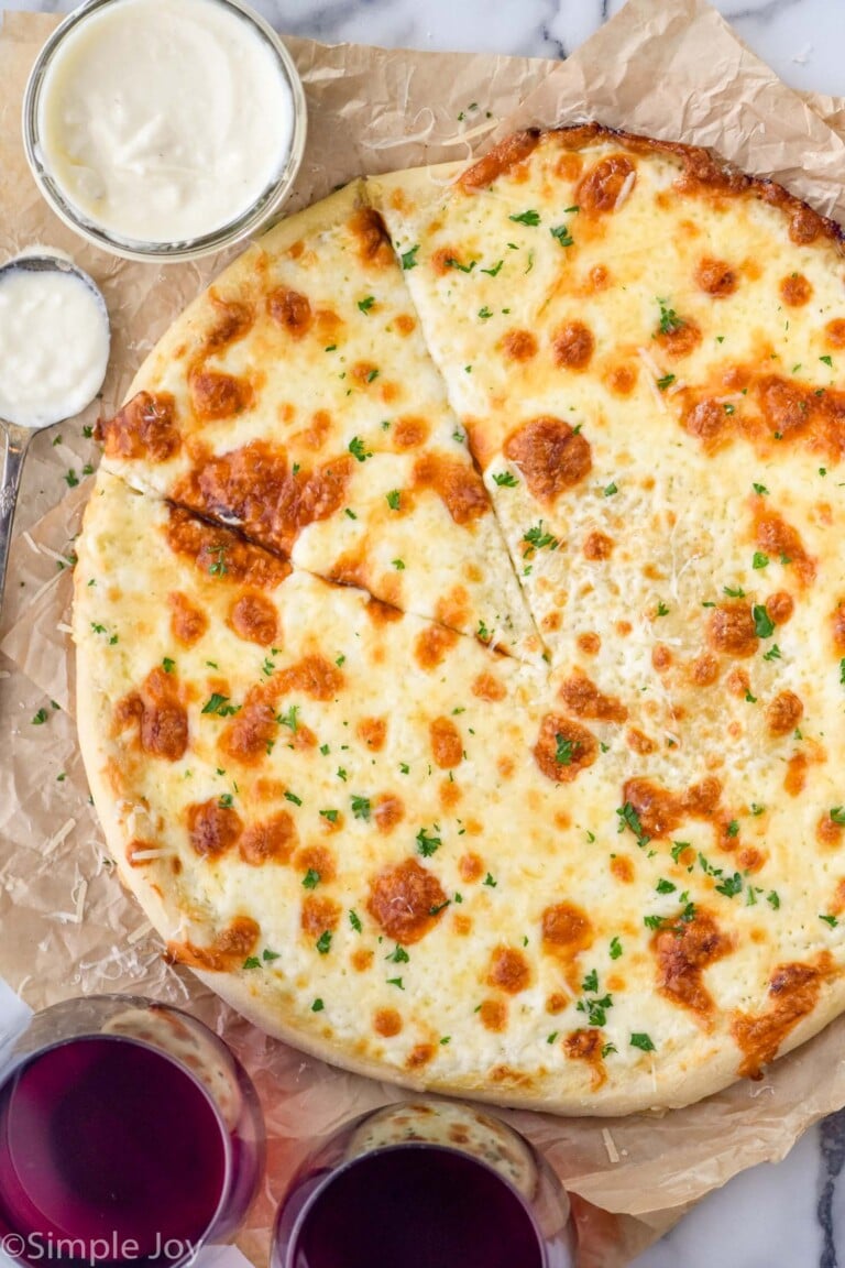 overhead of pizza with white pizza sauce. White sauce and two glasses of red wine sitting beside pizza