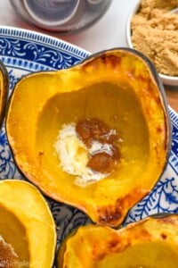 Roasted Acorn Squash on a plate. Bowl of brown sugar sitting beside