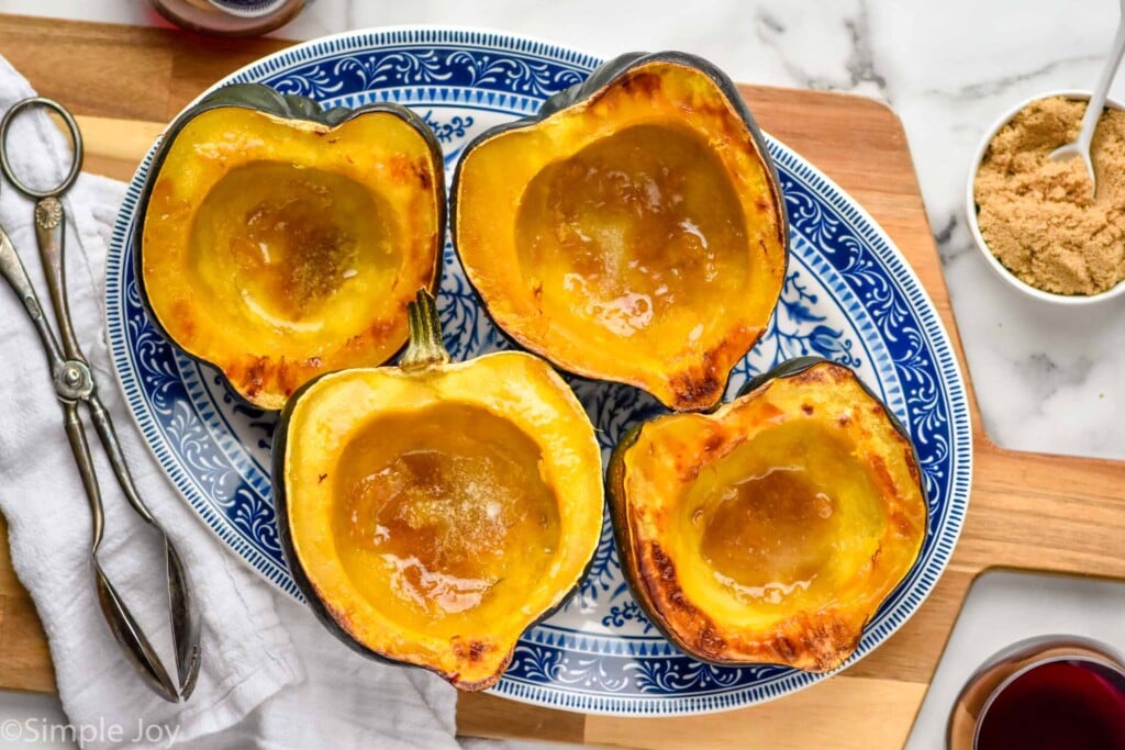 overhead of Roasted Acorn Squash on a plate with servings tongs and brown sugar sitting beside