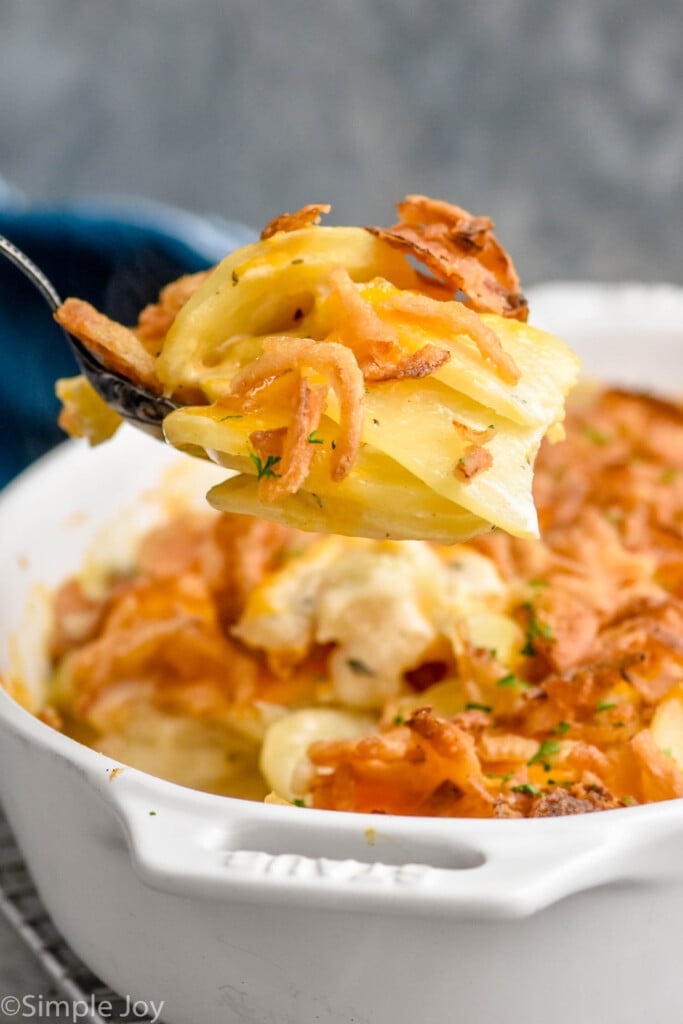Photo of a spoonful of Scalloped Potatoes over a baking dish of Scalloped Potatoes recipe
