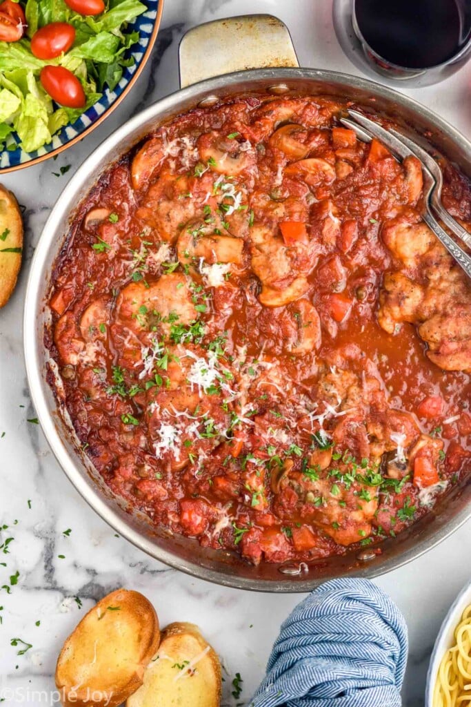 overhead of pan of Chicken Cacciatore. Garlic bread and bowl of salad sitting beside