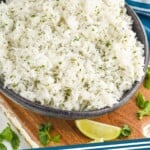 Pinterest graphic for Cilantro Lime Rice recipe. Image shows a bowl of Cilantro Lime Rice with limes, cilantro, and two margaritas beside. Text says, "Cilantro Lime Rice simplejoy.com"
